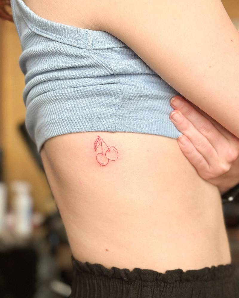 Fine line style red cherries tattoo located on the rib.