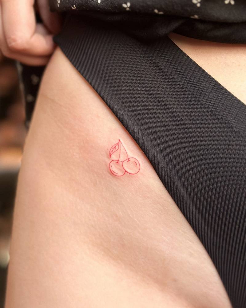 Fine line style red cherries tattoo done on the pelvis.