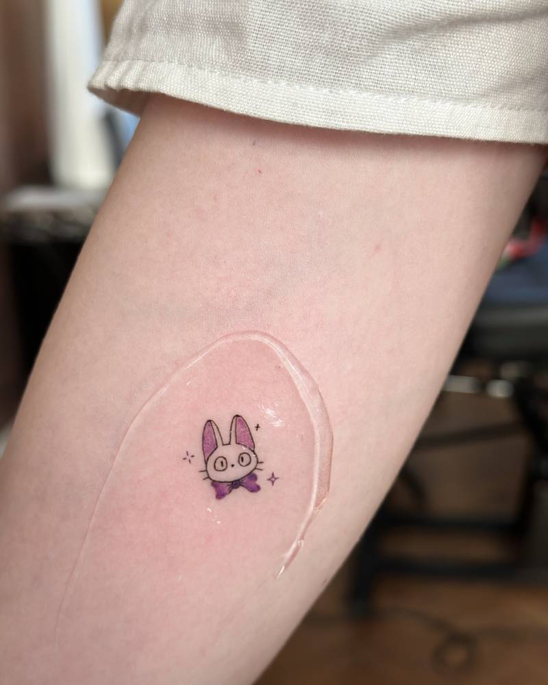 Tiny Jiji portrait tattoo located on the inner forearm, cartoon style.