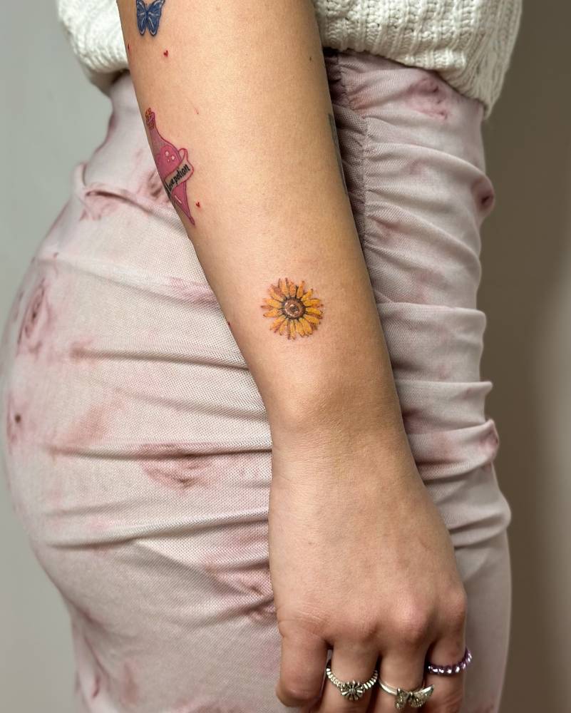 Sunflower tattoo located on the wrist, done in watercolor style.