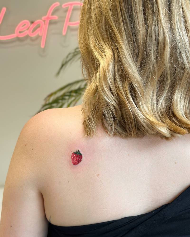 Little strawberry tattoo in illustrative style placed on the shoulder blade.