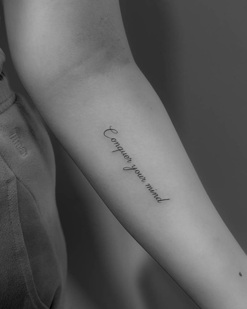 Script font "conquer your mind" tattoo located on the inner forearm.