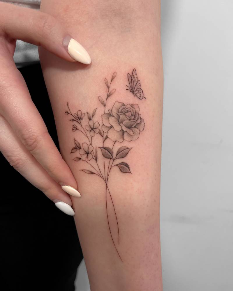 Illustrative style flower bouquet and butterfly tattoo located on the inner forearm.