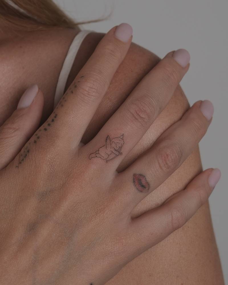 Fine line style little cupid tattoo located on the finger.