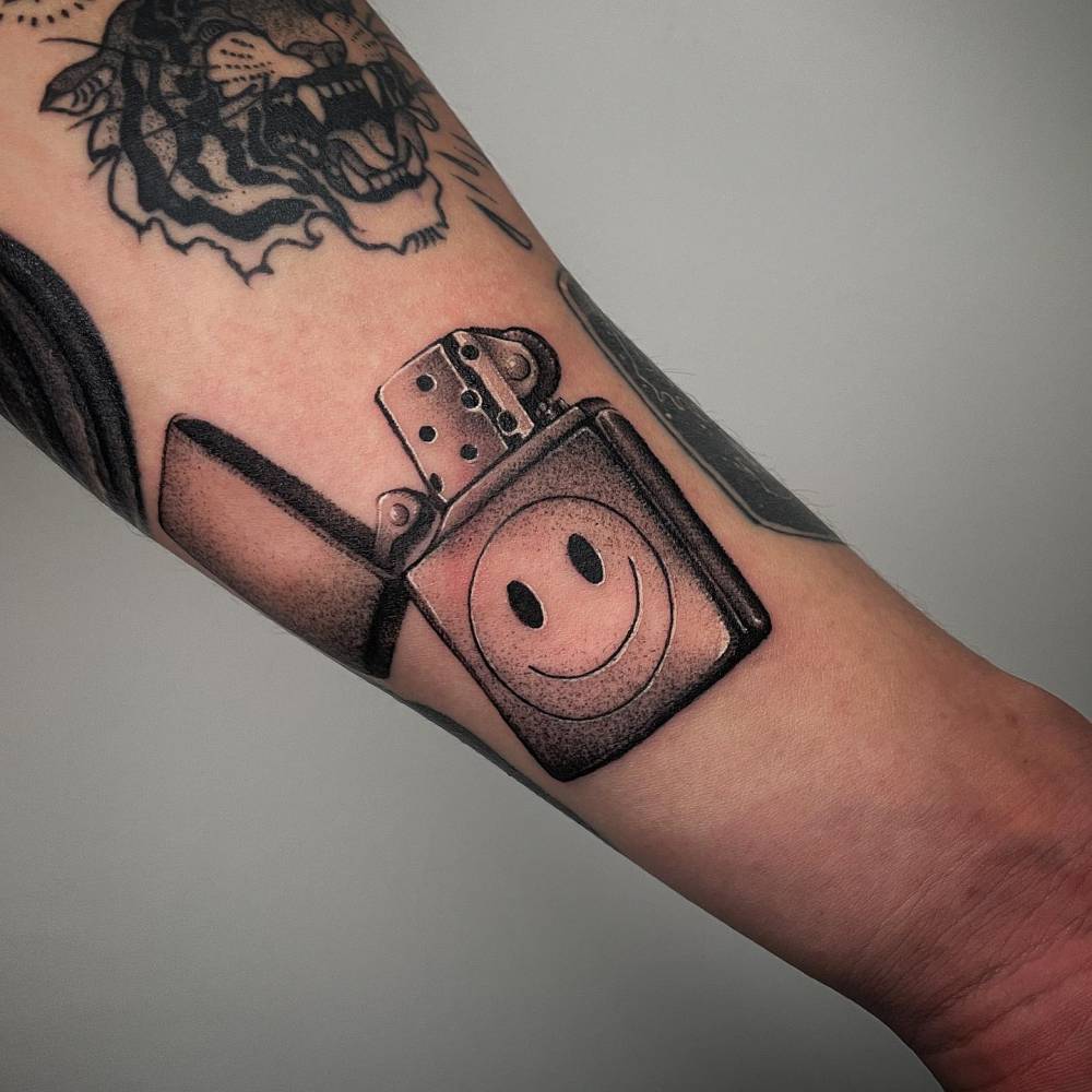 Smiley lighter tattoo in dotwork style placed on the wrist.