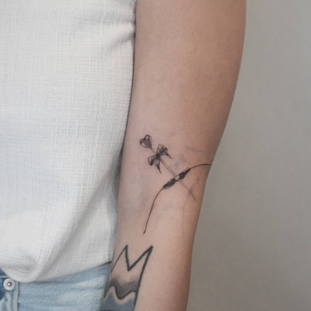 Illustrative style bow and arrow tattoo located on the arm.