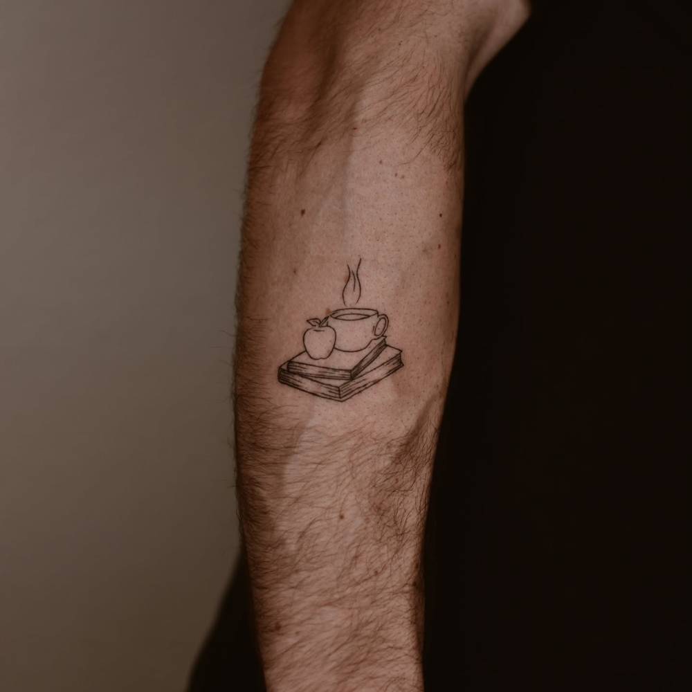 Coffee cup, books and apple tattoo located on the forearm, fine line style.