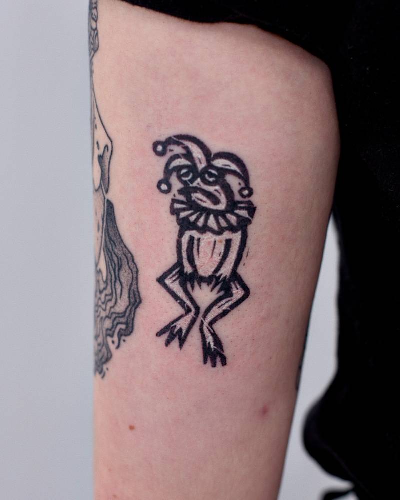 Jester frog tattoo located on the upper arm, pop art style.