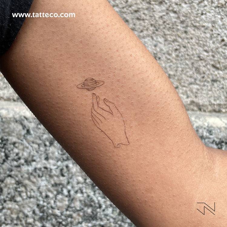Small fine line hand and Saturn temporary tattoo designed by Jakenowicz, get it here â–º http://bit.ly/3k9gxk0