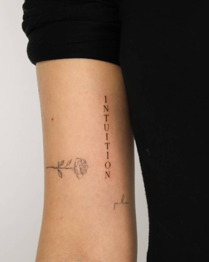 Serif font word "intuition" tattooed on the inner arm.