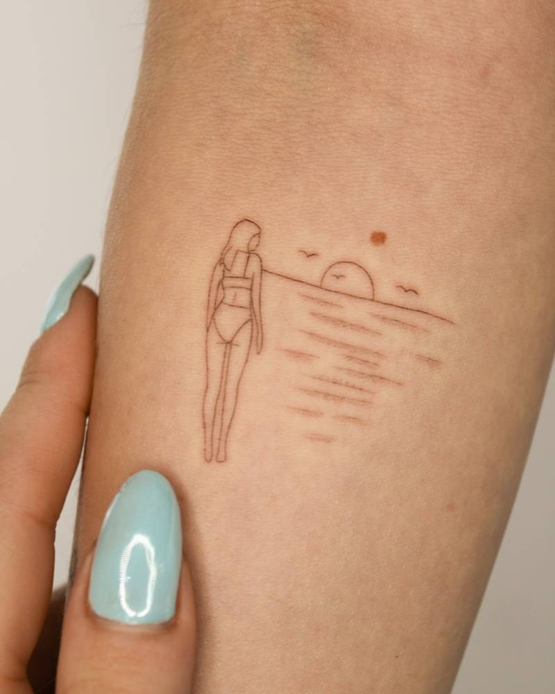 Woman and sea sunset tattoo in fine line style placed on the inner forearm.