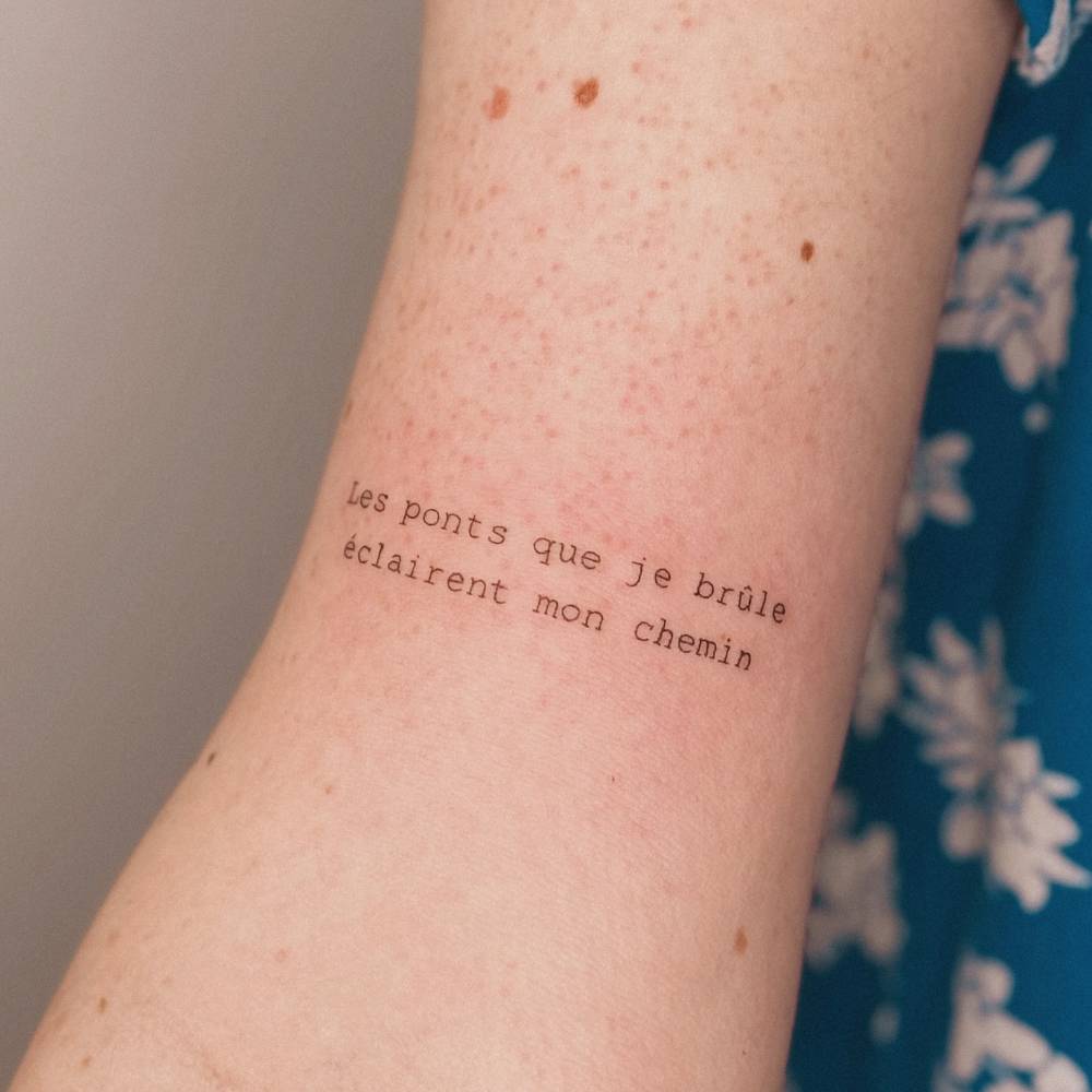 "Les ponts que je brule éclaire mon chemin" lettering tattoo located on the bicep.