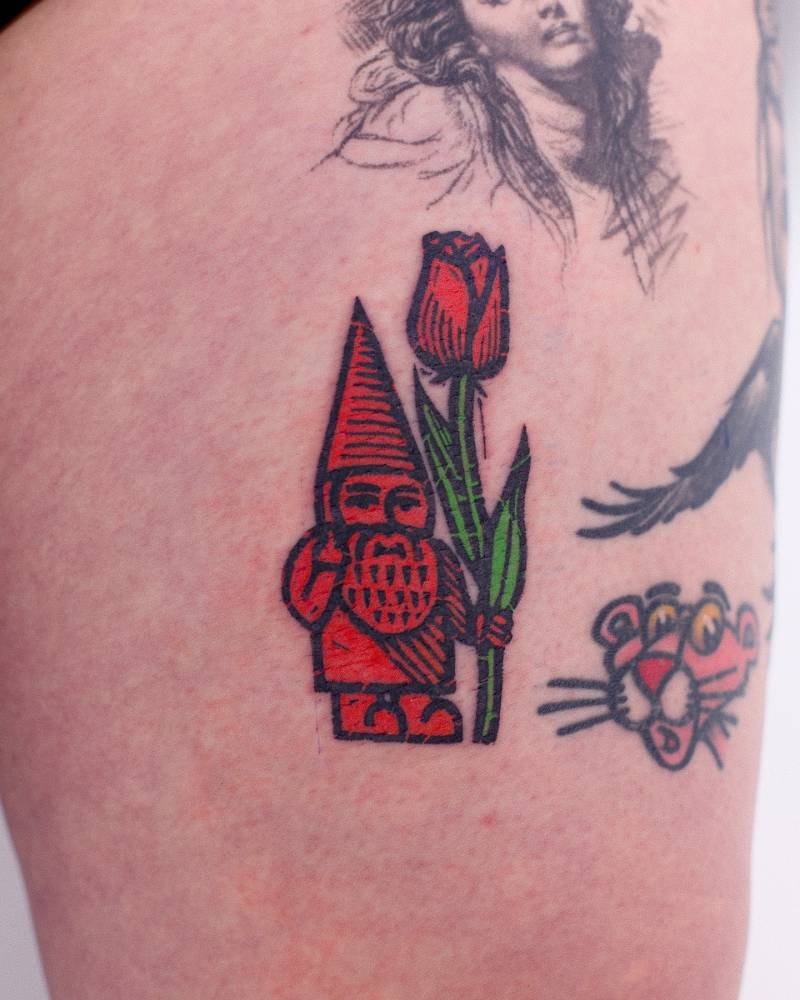 Pop art style gnome and red rose tattoo located on the thigh.
