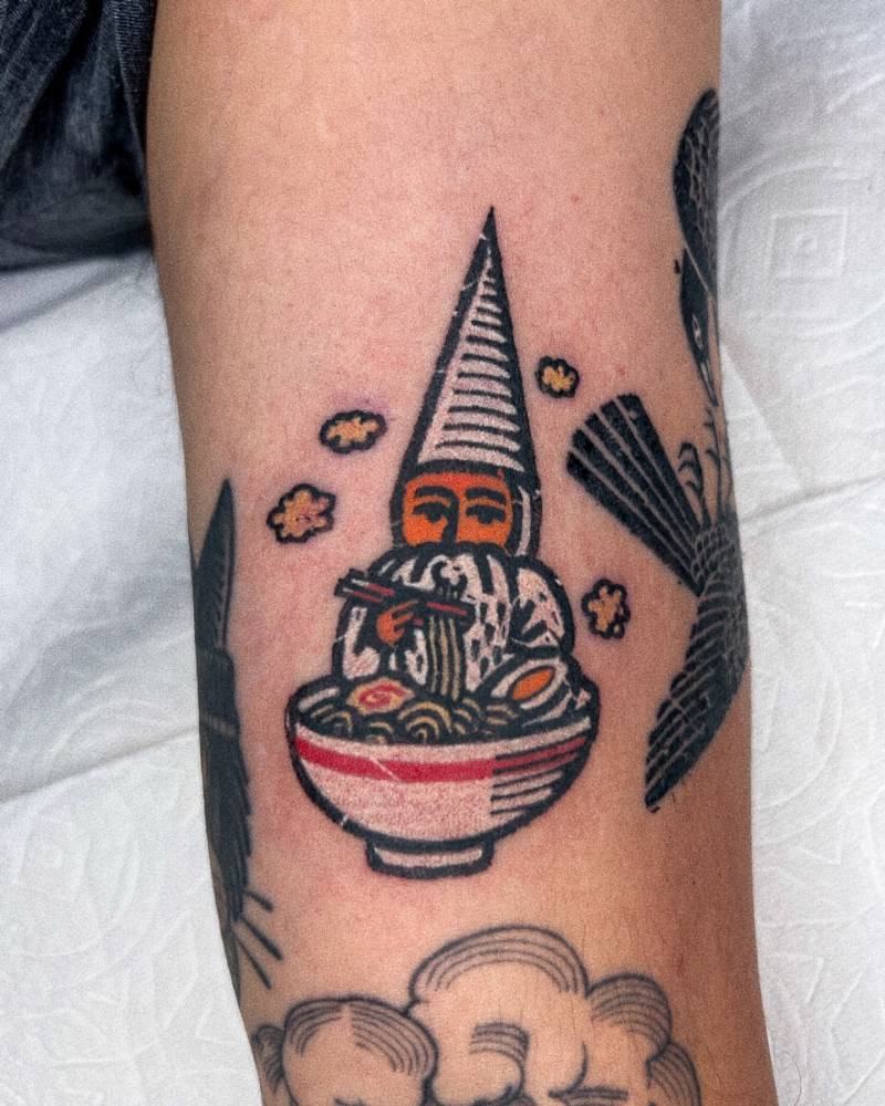 Gnome eating ramen tattooed on the upper arm.