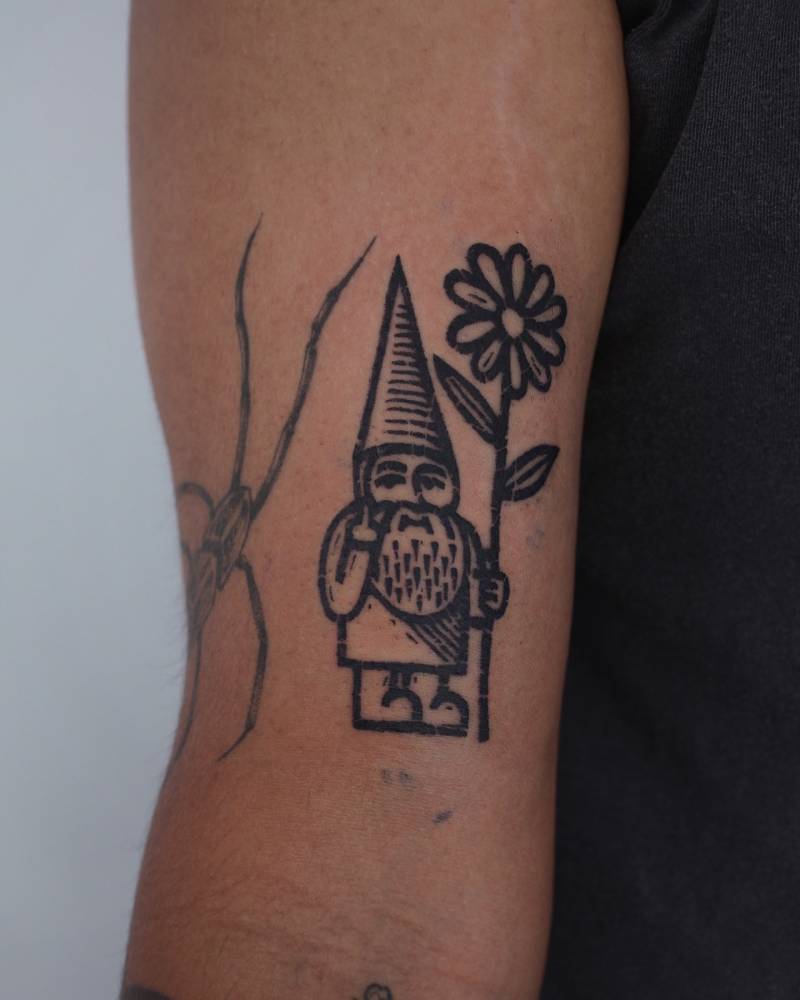 Gnome and daisy flower tattoo located on the bicep.