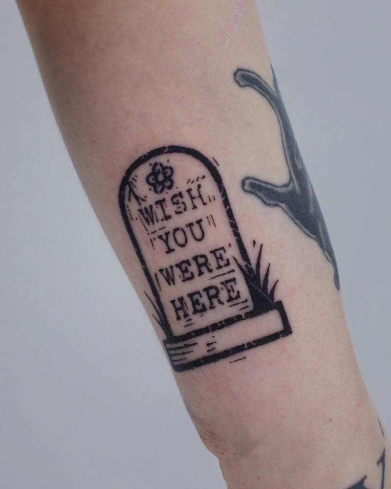 Headstone and words "wish you were here" tattooed on the wrist.