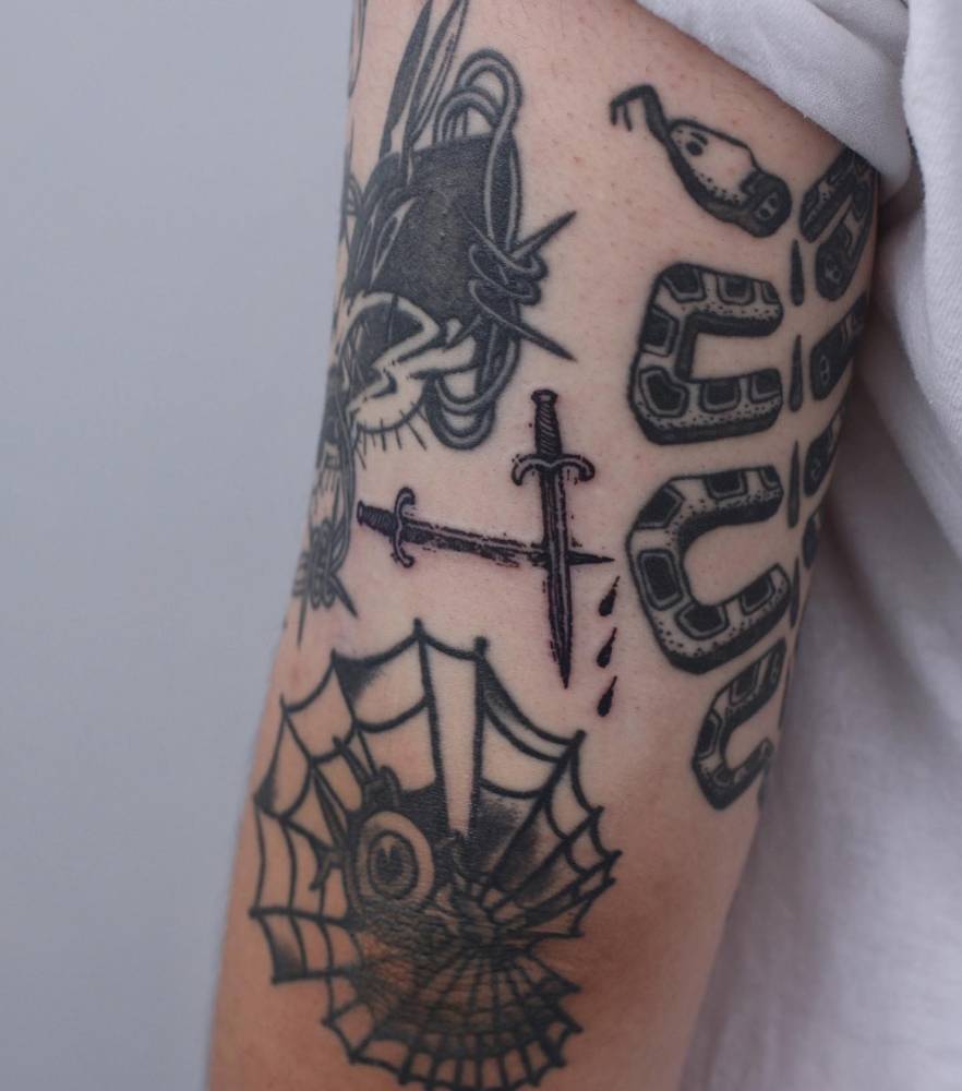 Little swords gap filler tattoo in blackwork style located on the tricep.