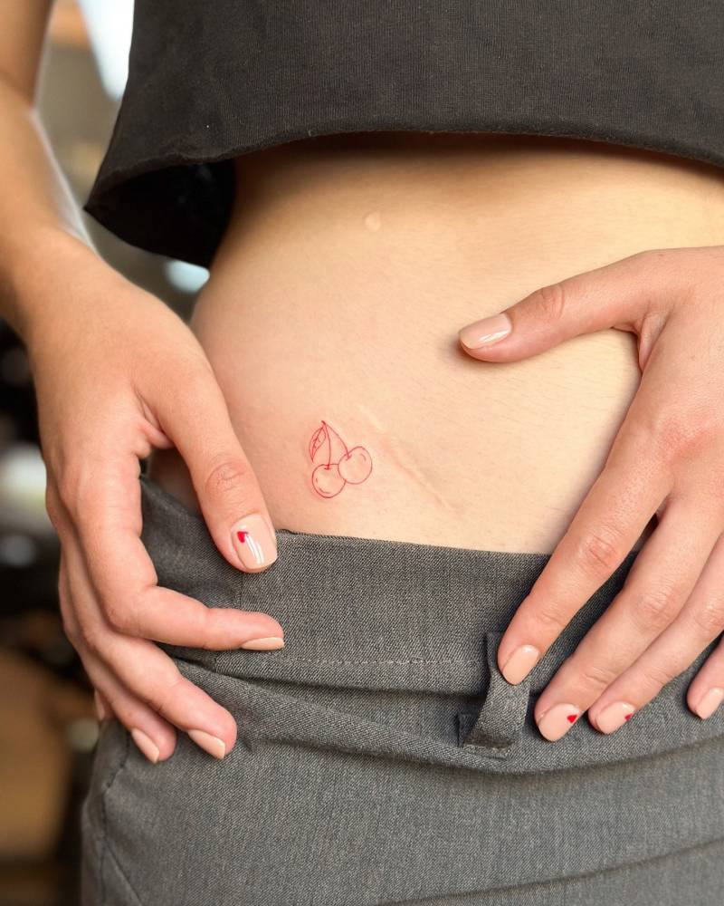 Fine line style cherries tattoo in red ink located on the pelvis.