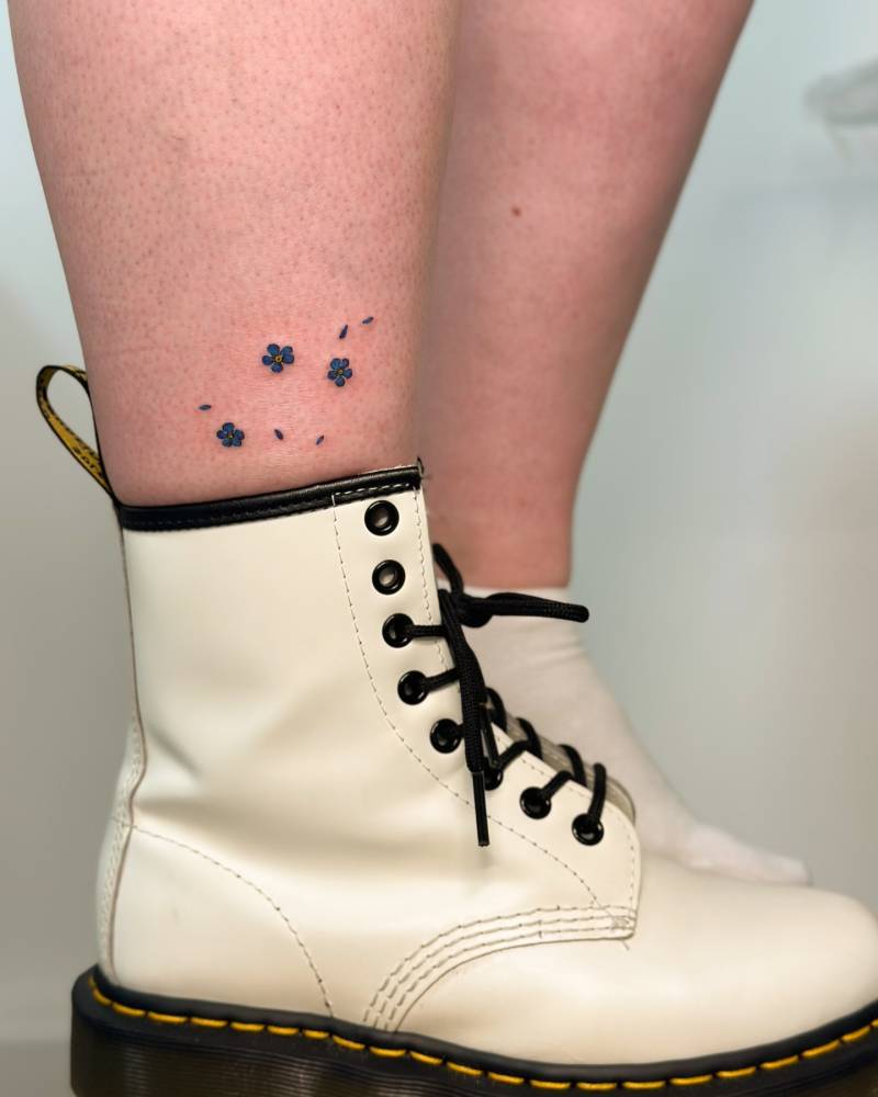 Watercolor style forget-me-not flowers tattooed on the shin.