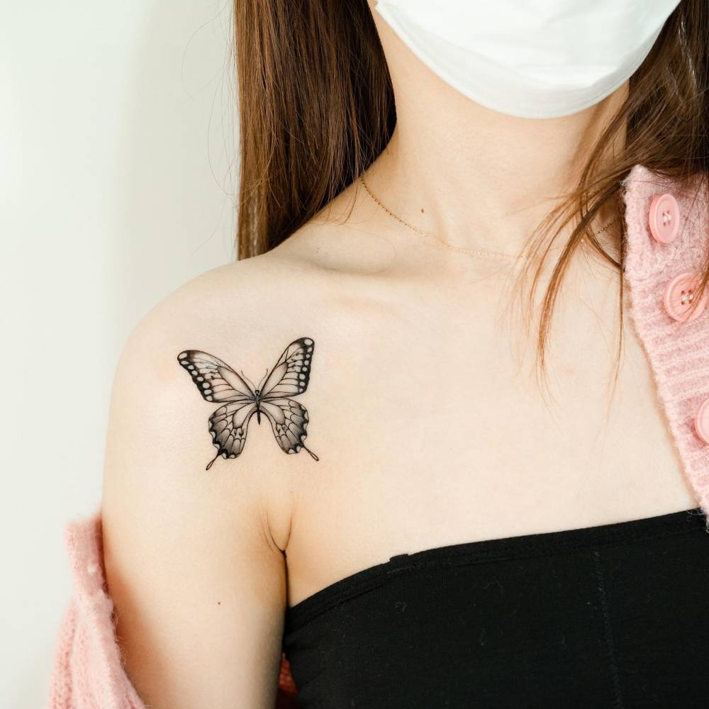 Butterfly tattoo located on the shoulder, illustrative style.