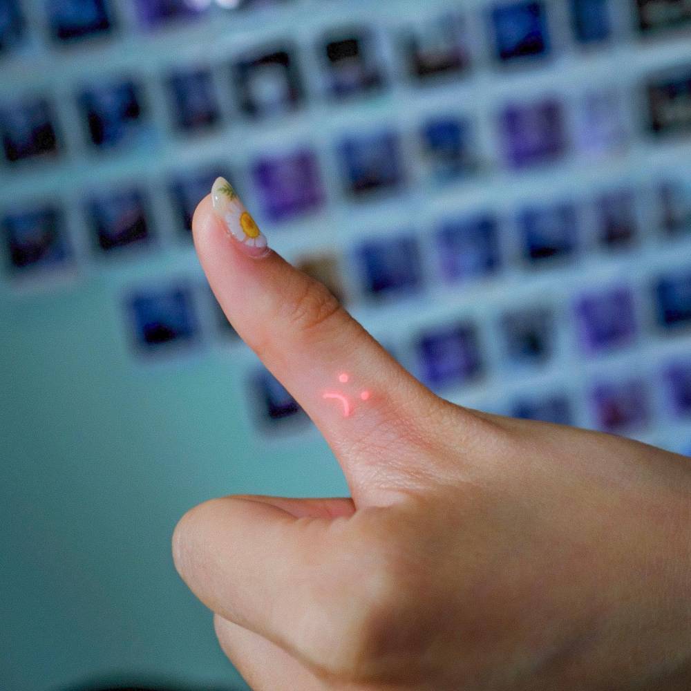 UV ink sad face tattoo located on the thumb.
