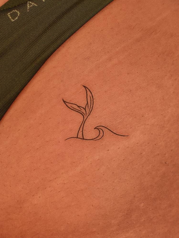 Mermaid tail and wave tattoo located on the pelvis, fine line style.