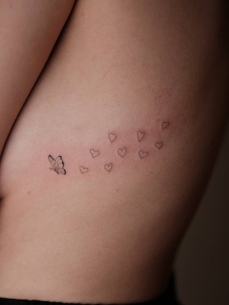 Butterfly and hearts tattoo in fine line style placed on the rib.