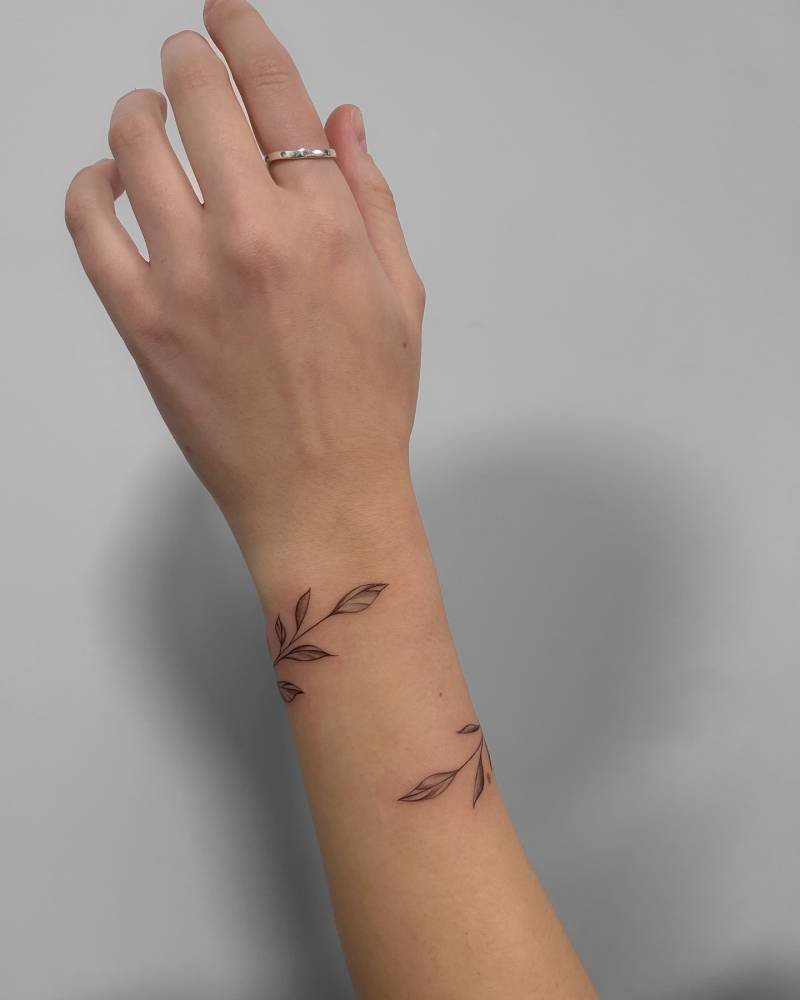 Leaves bracelet tattoo in illustrative style located on the wrist.