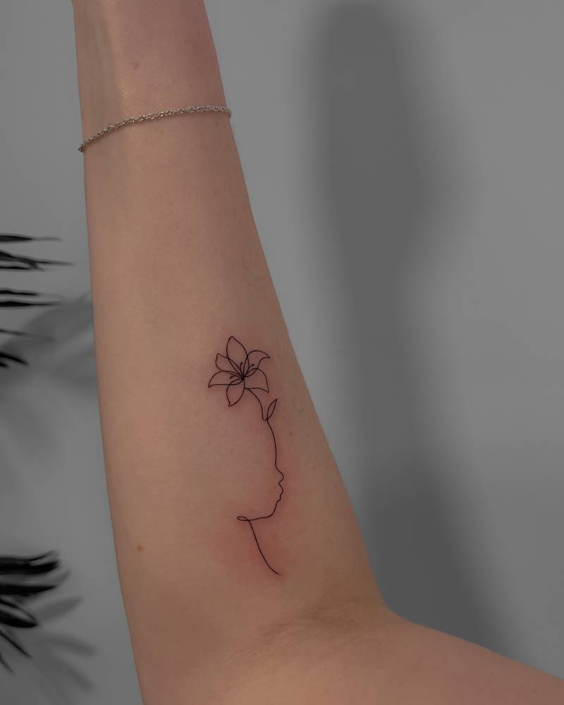 Fine line style lily flower and baby face tattoo located on the inner forearm.