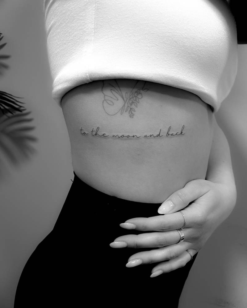Handwritten font "to the moon and back" lettering tattoo placed on the rib.