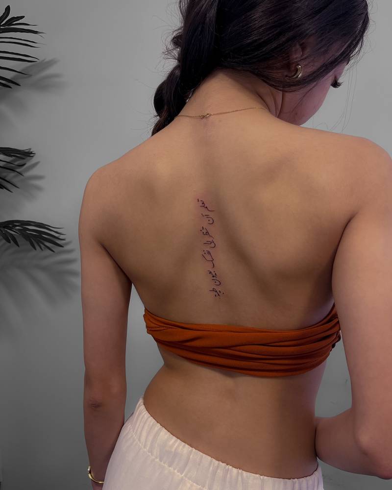 Arabic lettering tattoo located on the upper back.