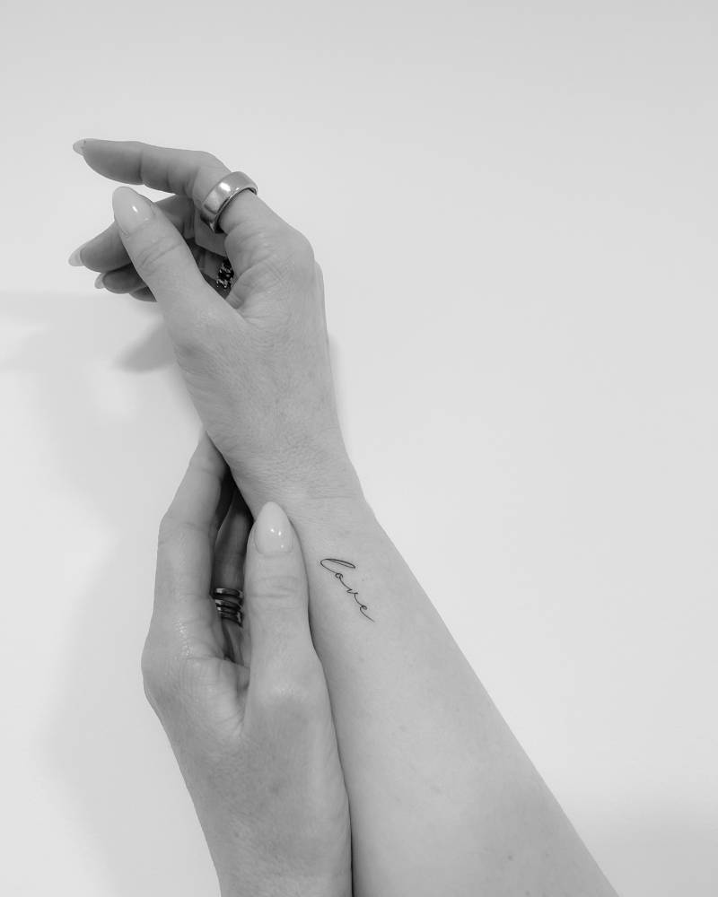 Lettering tattoo of the word "love" handwritten on the wrist.