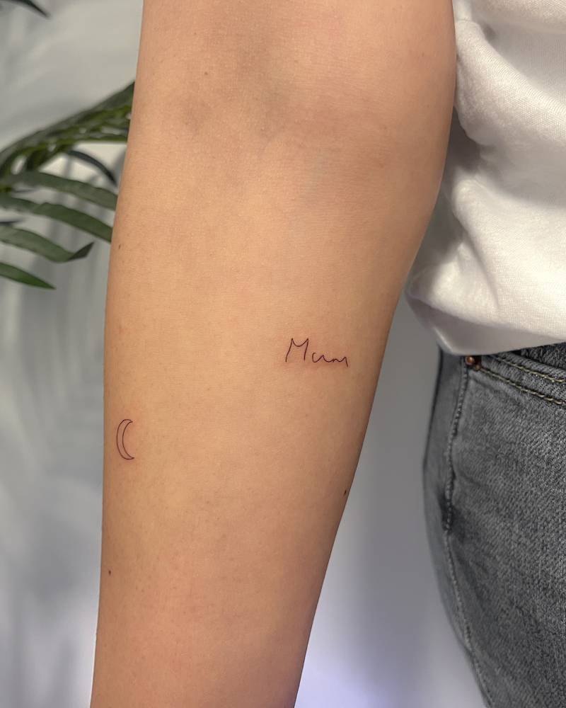 "Mum" and crescent moon tattoos located on the inner forearm.