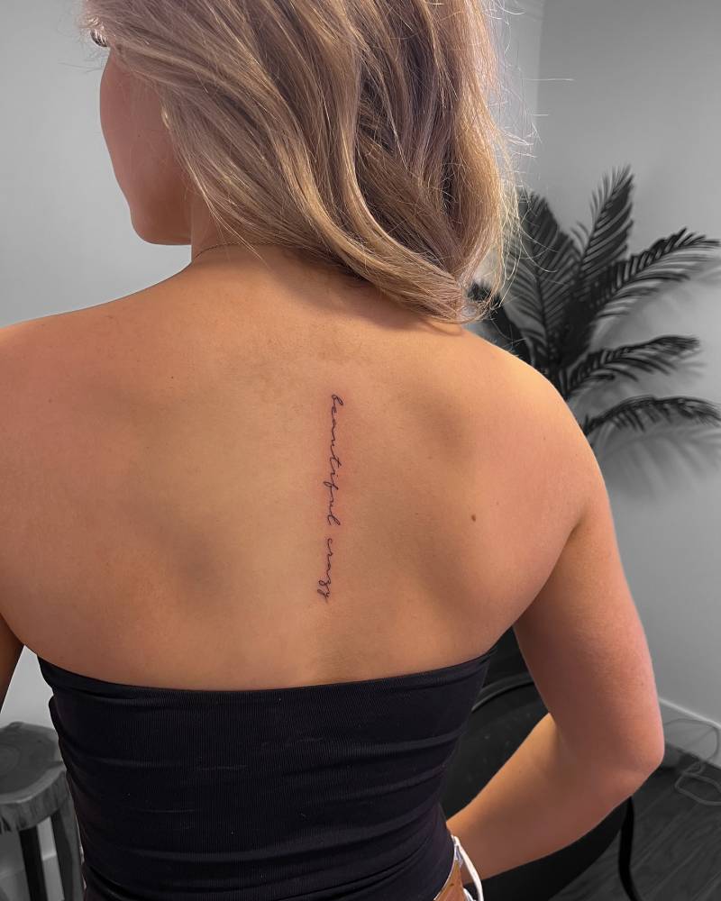 Handwritten lettering tattoo that says "beautiful crazy" located on the upper back.