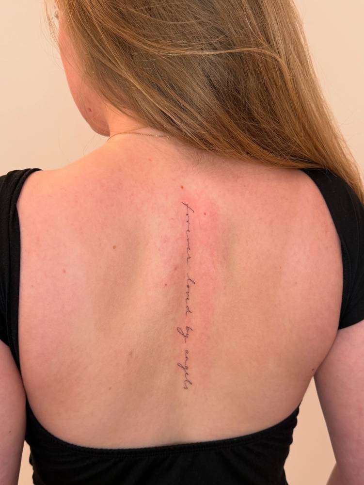 "Forever loved by angels" lettering tattoo located on the spine.