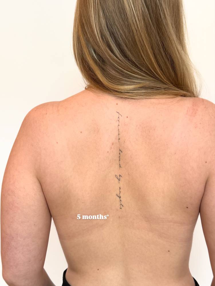 6 months healed "forever loved by angels" lettering tattoo located on the spine.