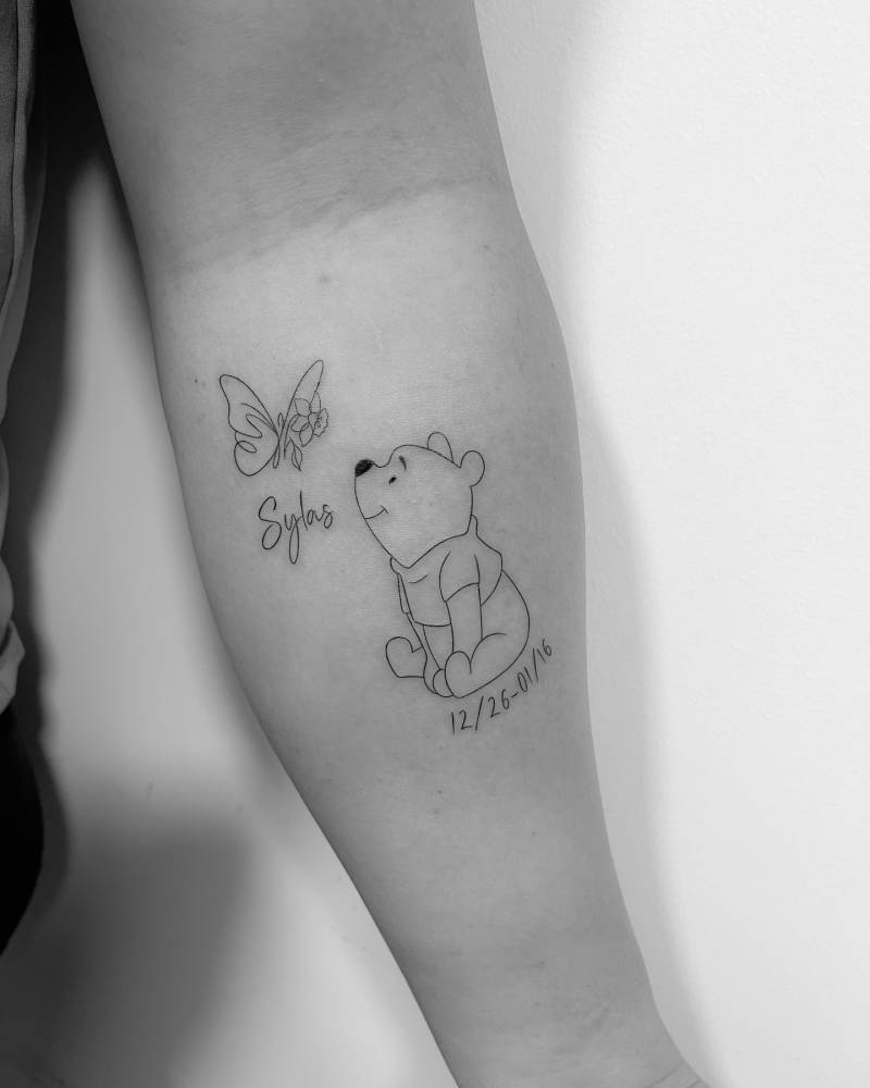Pooh Bear and butterfly tattoo in fine line style located on the inner forearm.