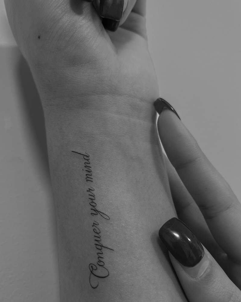 Script font "conquer your mind" lettering tattoo located on the wrist.