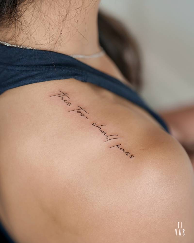 "This too shall pass" lettering tattoo located on the top of shoulder.