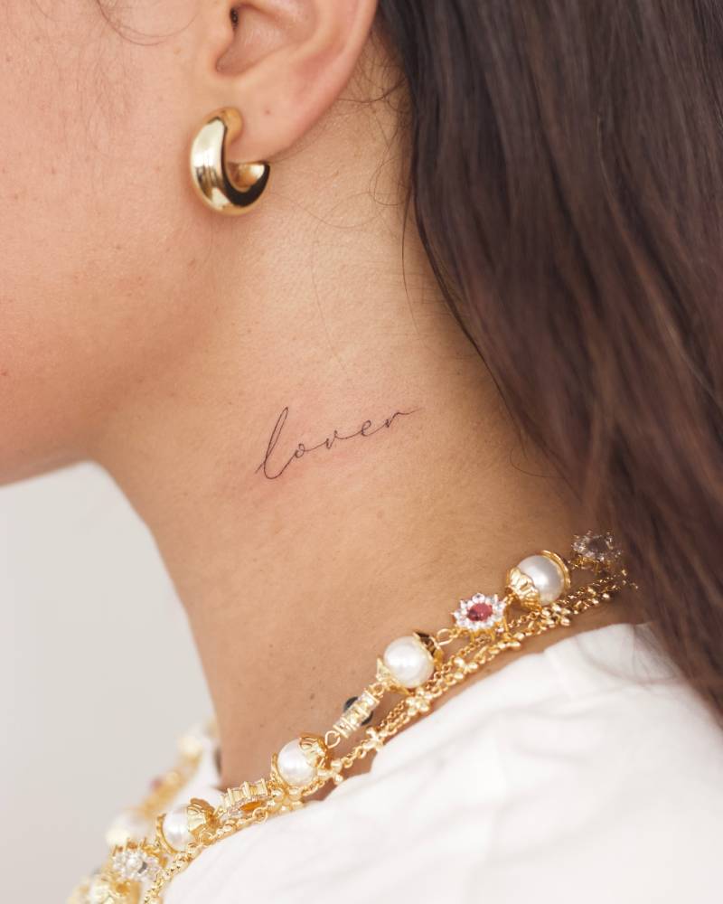 Lettering tattoo of the word "lover" located on the neck.