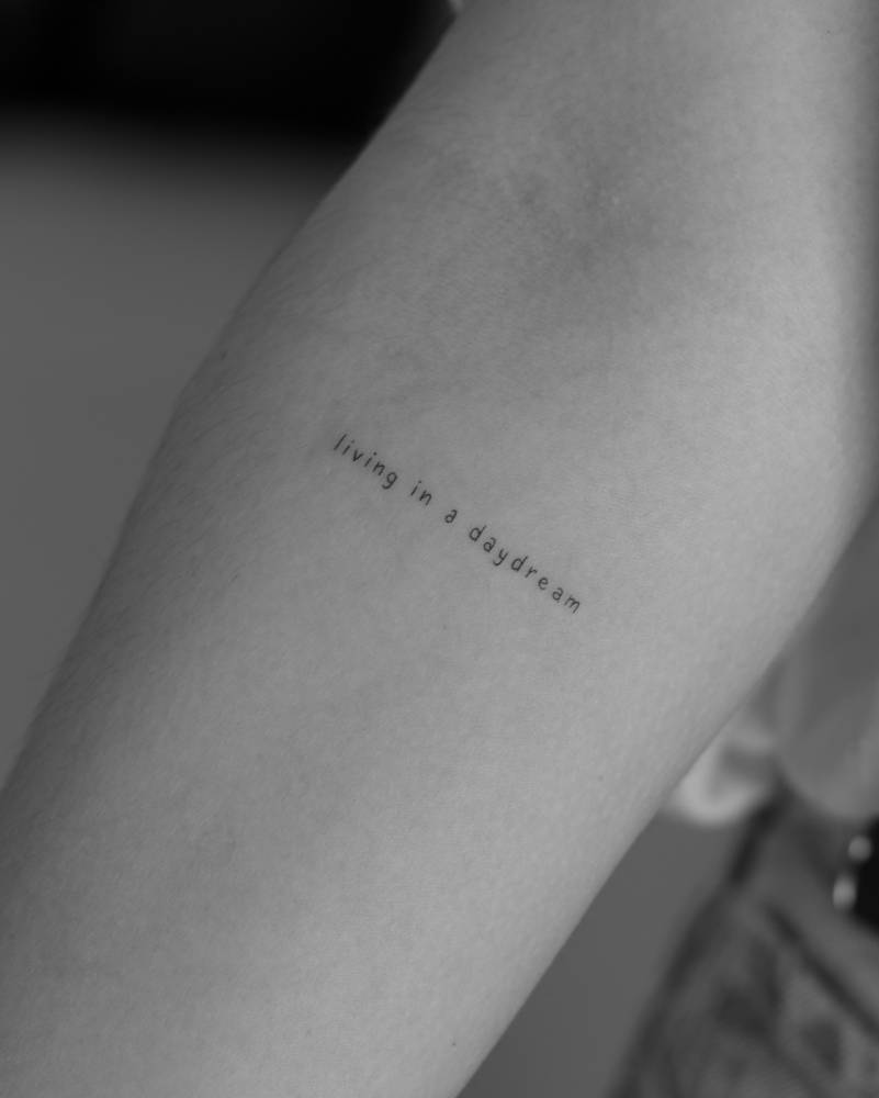 "Living in a daydream" lettering tattoo placed on the inner forearm.
