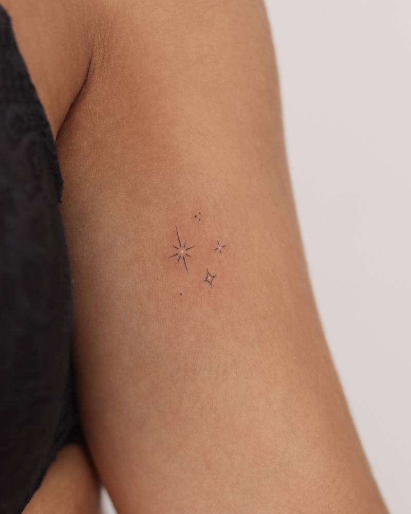 Sparkling stars tattoo in minimalistic style located on the bicep.