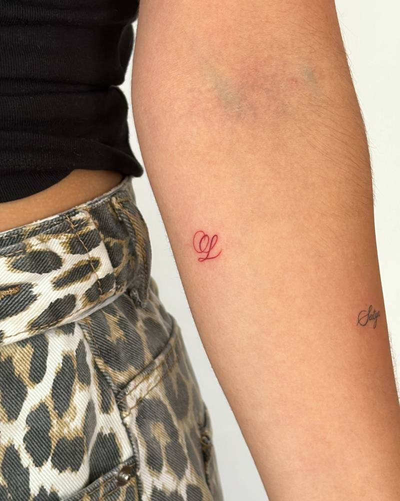 Script font letter "L" tattoo located on the inner forearm.