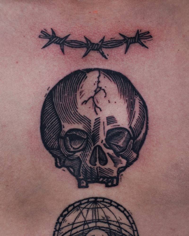 Engraving style skull and barbed wire tattoo located on the chest.