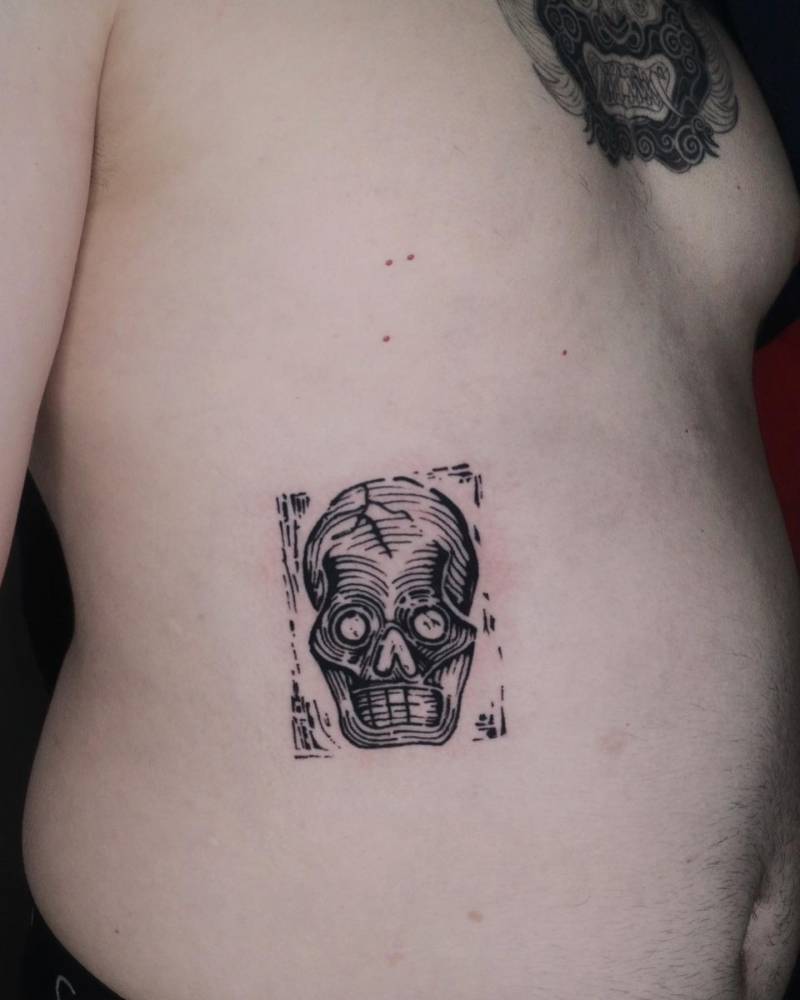 Skull tattoo located on the rib, done in blackwork style.