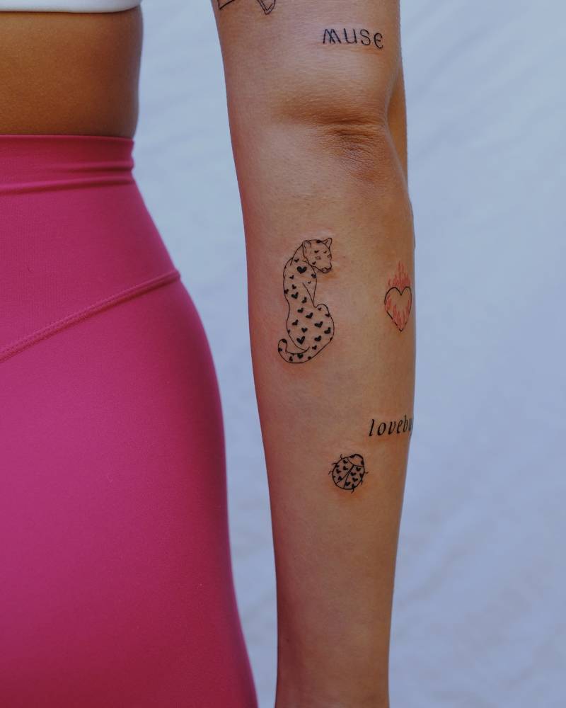 Leopard and ladybug tattoos in illustrative style located on the forearm.