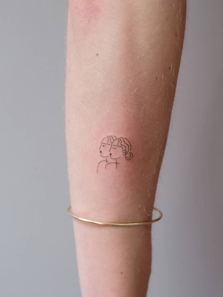 Minimalistic tattoo of two women located on the forearm.