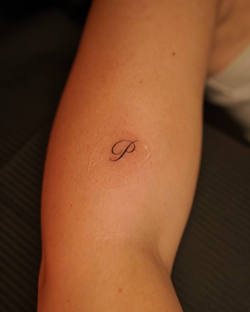 Little letter "P" tattoo located on the upper arm.