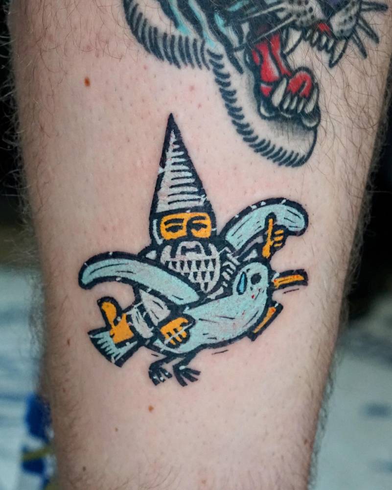 Gnome riding a seagull tattooed on the shin, pop art style.