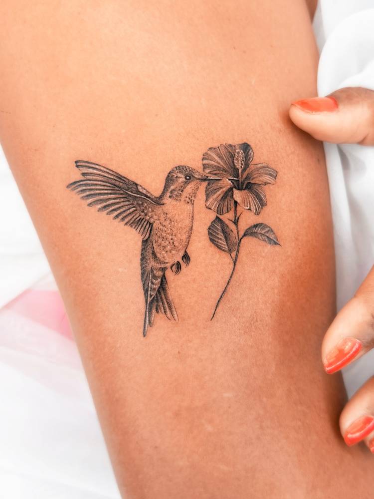 Micro-realistic style hummingbird and hibiscus flower tattooed on the upper arm.